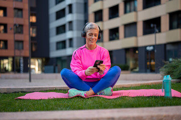 Mature woman relaxing on yoga mat with smartphone