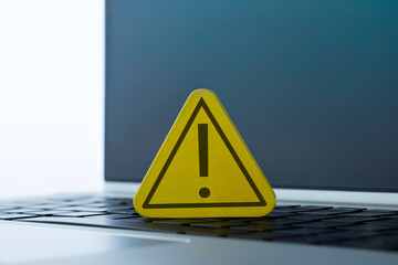 A yellow warning sign with an exclamation mark placed on a laptop. Cybersecurity, computer error, system alert, online danger concept.
