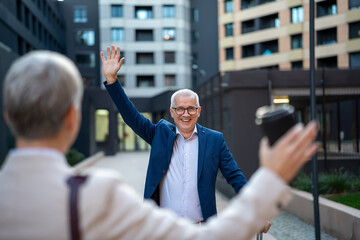 Mature businessman waving hands greeting a colleague outdoors