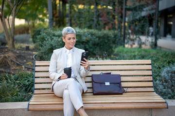 Elegant businesswoman using smartphone during outdoor coffee break
