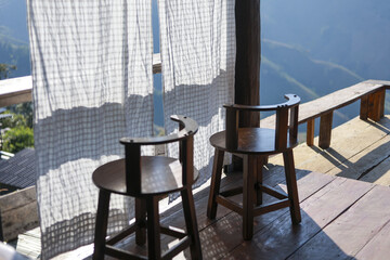 Obraz premium Two empty wooden chairs on rustic porch create relaxing and peaceful outdoor scene. Sunlight shines on simple furniture and white curtain, perfect for calm morning at cafe