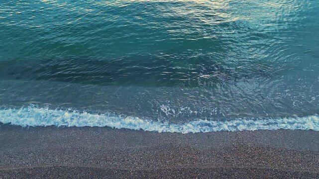 Drone footage of calm waves on coast with a relaxing atmosphere showing the gentle rhythm of the sea as it washes over the pebbles creating a peaceful nature loop for backgrounds