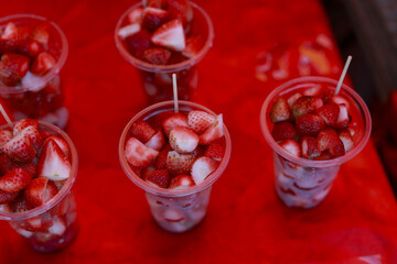 Delicious fresh strawberry dessert in plastic cup on red background. Sweet fruit snack, healthy and refreshing treat, perfect for summer food at vibrant market stall