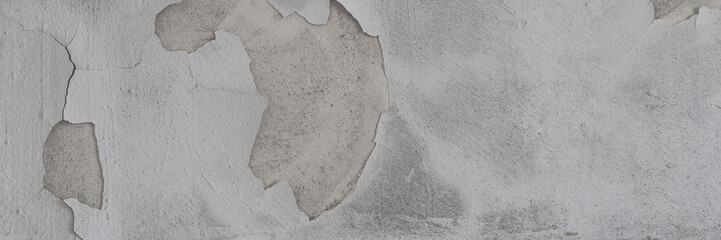 Peeling paint on the wall. Panorama of a concrete wall with old cracked flaking paint. Weathered rough painted surface with patterns of cracks and peeling. Wide panoramic texture for design background
