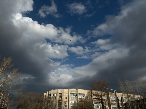 Dramatic dark clouds gather over a city apartment building and bare trees