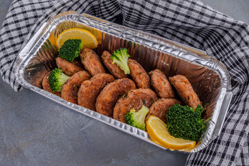 Salmon patties with lemon and broccoli in a foil baking container