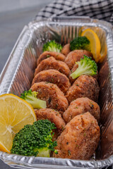 Salmon patties with lemon and broccoli in a foil baking container