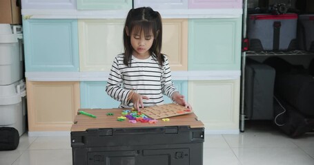 A young girl intently focuses on an educational activity, placing colorful letter and number pieces into a wooden puzzle board