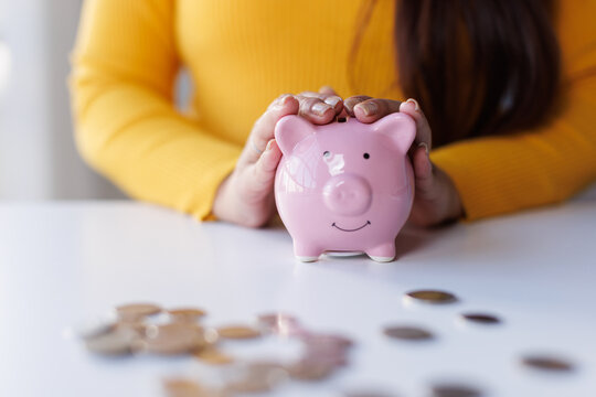 Saving money wealth concept, asian business woman hand putting coin into piggy for saving cost, cash finance planning to spend enough money on her income for save money, payment tax, investing.
