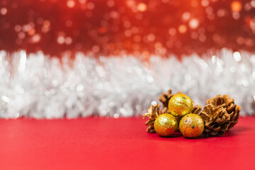 Christmas golden balls and pine cones over a red surface. There is a silver garland and snowy red blurred background.