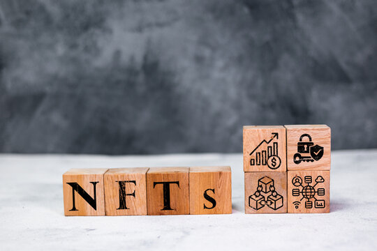 Wooden blocks spelling “NFTs” stand beside icons representing blockchain, finance, security, digital networks, illustrating the concept of non-fungible tokens in modern digital and crypto technology - Powered by Adobe