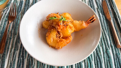 Two large, golden-fried tempura shrimp glazed with a creamy, spiced sauce and topped with herbs, served on a white plate