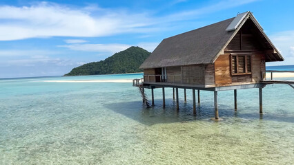 Rural wooden house on stilts above clear, shallow turquoise sea water with tropical island mountains in the background