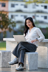 Young woman smiling while working on laptop outdoors