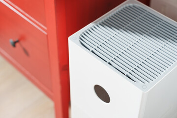 Close up white modern air purifier in the bedroom, living room by cozy wooden red chest of drawer...