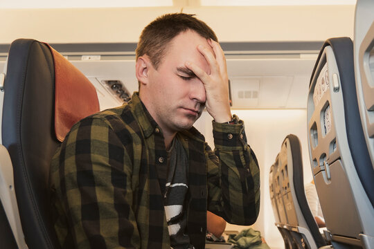 concept of health problems during an airplane flight. Aerophobia, fear of flying. Young man is flying in airplane and holding sore head