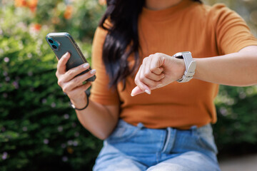 Woman checking smartwatch, holding mobile phone outdoors