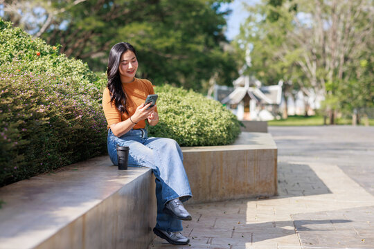 Young asian woman using smartphone in park - Powered by Adobe