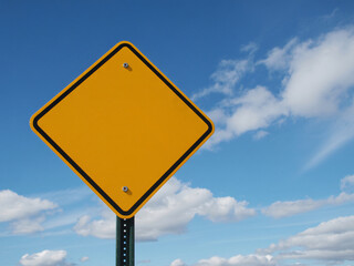 Vibrant blank yellow street sign against a bright blue sky with fluffy clouds inviting customization and perfect for your message