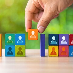 A hand places a colorful wooden block with a person icon onto a growing stack of similar blocks