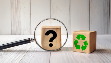 Magnifying Glass Zooming on Wooden Block with Question Mark Next to Recycling Symbol on Wood Table