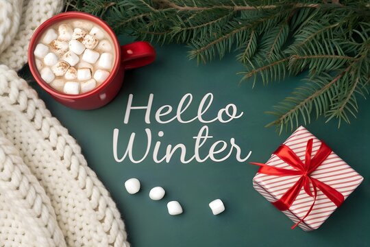 Cozy hello winter scene with hot chocolate and marshmallows a festive gift box and evergreen branches evoking warmth and holiday spirit on a dark background