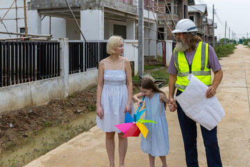 Senior construction foreman with beard using blueprint to explain a mother and her daughter for the...