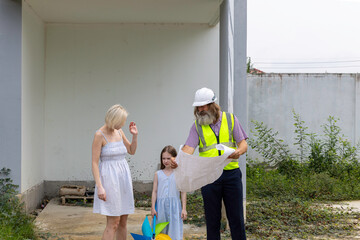Senior construction foreman with beard using blueprint to explain a mother and her daughter for the...