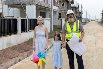 Senior construction foreman with beard using blueprint to explain a mother and her daughter for the...
