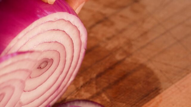 Slow-motion close-up in horizontal format showing a red onion as a thin ring is cut off with a sharp blade. The crisp layers and smooth motion emphasize precision and vibrant texture.