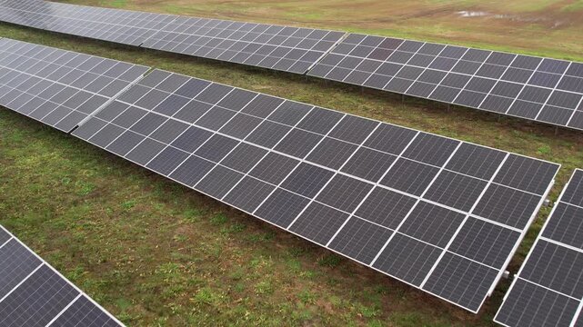 Rows of large solar panels aligned across a grassy field, viewed from above, capturing a renewable energy installation under overcast skies.