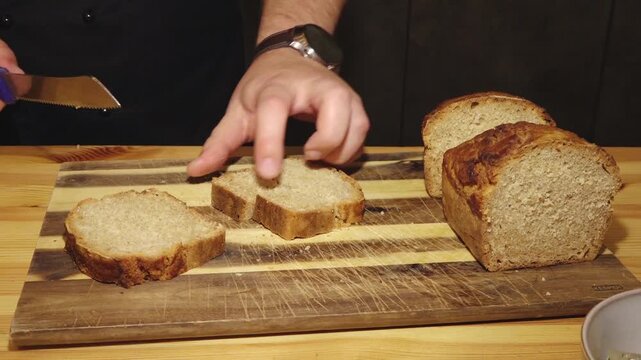 A person uses a serrated knife to slice loaves of fresh homemade bread on a rustic wooden cutting board.