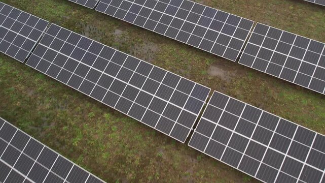 Rows of large solar panels aligned across a grassy field, viewed from above, capturing a renewable energy installation under overcast skies.