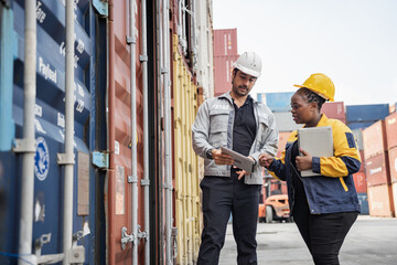 Man and woman logistics workers in high visibility safety gear discuss operations and checking container at shipping container yard	
