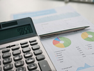 Financial calculations with a calculator, pen, and charts on a desk for budget analysis concept