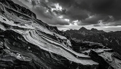 Black and white landscape featuring layered rock formation, mountains, and stormy sky