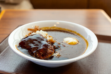 Japanese curry rice bowl, featuring a rich, dark brown sauce and a large hamburg steak or katsu cutlet.