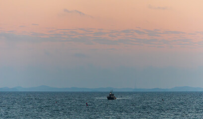Fototapeta premium A Boat Passing Over the Sea Under an Orange Sunset Sky