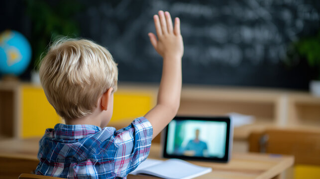 Rear view of a young schoolboy raising his hand during an online lesson on a tablet