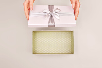 Female hands opening an empty gift box adorned with a silver ribbon bow set against a warm Cloud Dancer gray color of 2026 year background capturing the essence of surprise and celebration from above