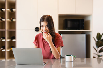 Asian woman in casual using laptop sit alone at table in kitchen at home, work or study.Housewife checking email on laptop.