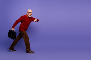 Mature man in red sweater with briefcase walking forward against purple background expressing joy...