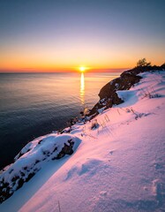 Winter sunrise over a snowy cliff overlooking a calm lake