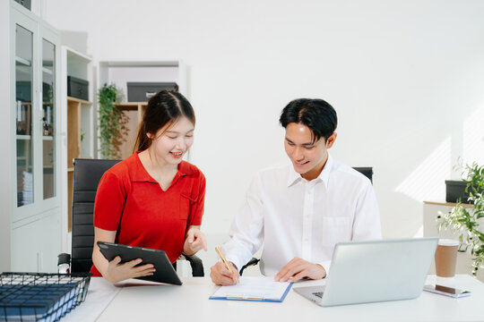Two Asian coworkers collaborating on business planning, discussing documents and using digital devices in modern office