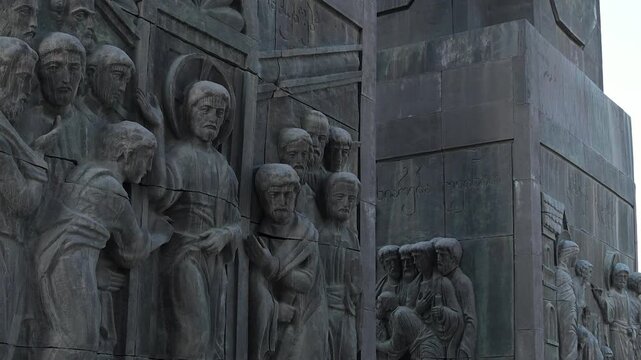 Visitors walk among the monumental sculptures at Chronicle of Georgia in Tbilisi highlighting human scale against dramatic carved pillars.