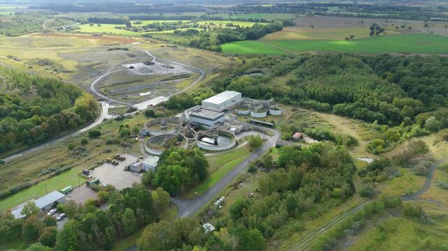 Drone view of wastewater treatment plant in Yorkshire UK showing clarifying tanks and industrial infrastructure surrounded by countryside fields and rolling hill