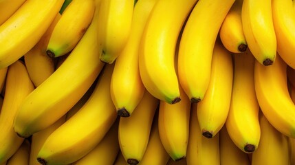 Bright yellow bananas stacked together create a fresh fruity background that suggests vibrancy and health in a market setting during daylight