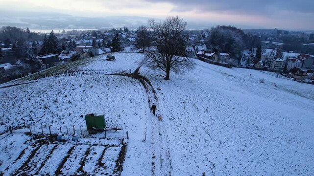 Aerial of a man walking on a snowy hill with a wood sledge, Uster, Switzerland