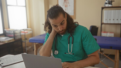 Man doctor in green scrubs with stethoscope rubbing his neck at clinic desk in medical building; fatigue neckache burnout.