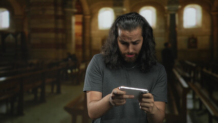 Man holds smartphone and grimaces while seated in church building, fingers gripping device and face contorted; distress.